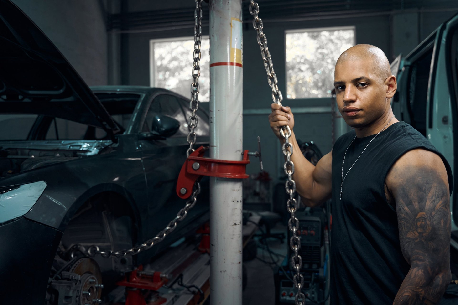 African American auto mechanic securing chains to raise vehicle for repair