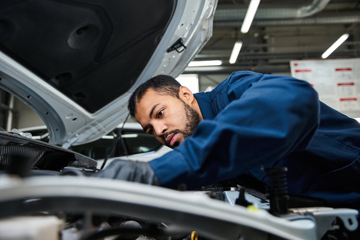 A young mechanic concentrates on car maintenance at a bustling auto repair service center