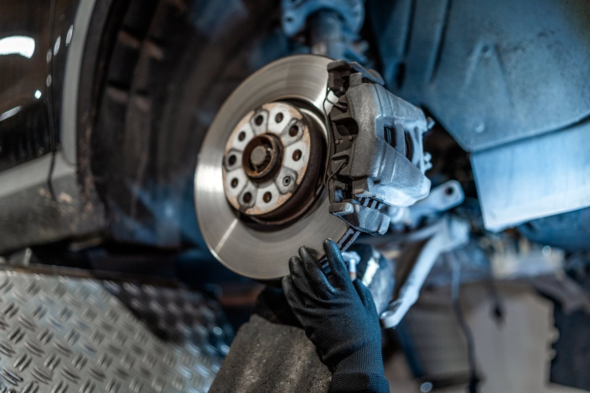 Close up of mechanic's hands wearing gloves, inspecting car brake disc and caliper during maintenance