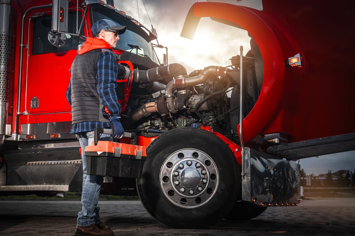 A truck driver inspects the engine of a big rig during sunset