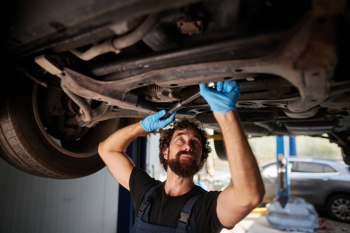 Mid adult mechanic working under a car held up by a hydraulic lift, using a wrench and wearing blue gloves
