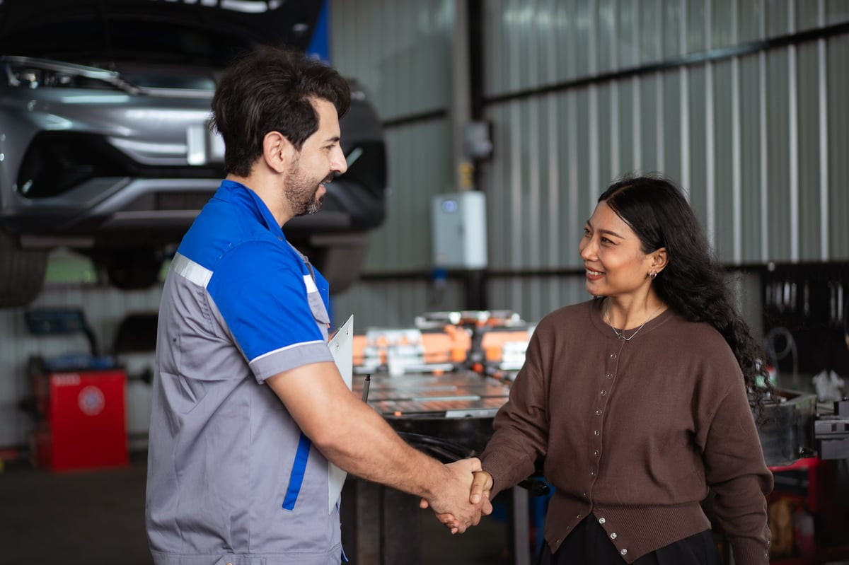 Male auto mechanic shaking hands with smiling female customer after completing car repair service inside workshop garage.
